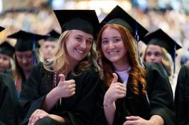 Two female 学生 give the thumbs up at commencement
